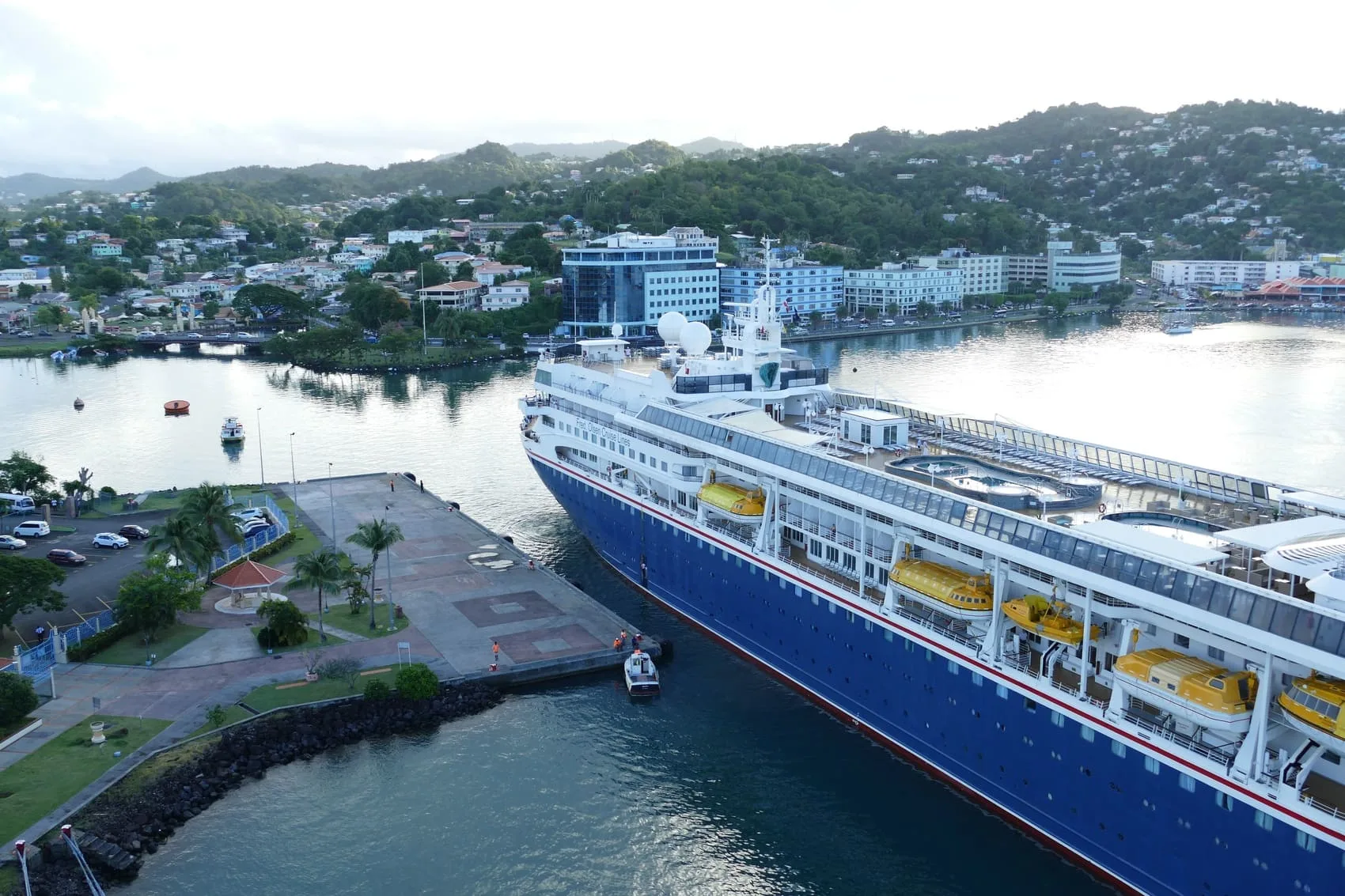 Aerial view of a Fred Olsen cruise ship docked in Castries harbor, Saint Lucia, with the city's hillside buildings and coastline in the background